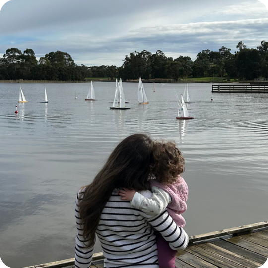 A mother holds her young child looking out at some yachts on the water.