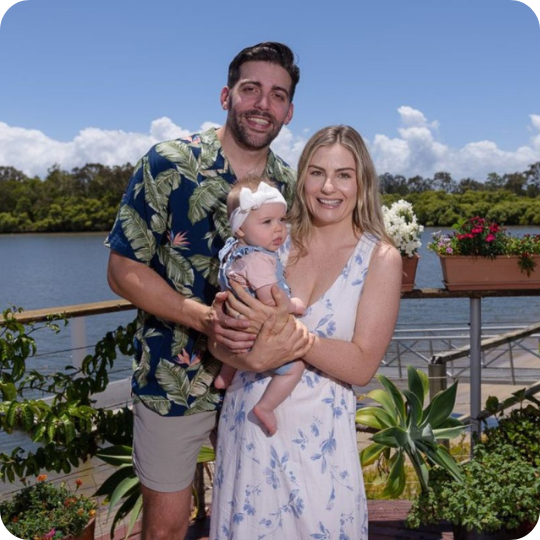 A portrait of Alexandra Gannon with her partner and baby in her arms.